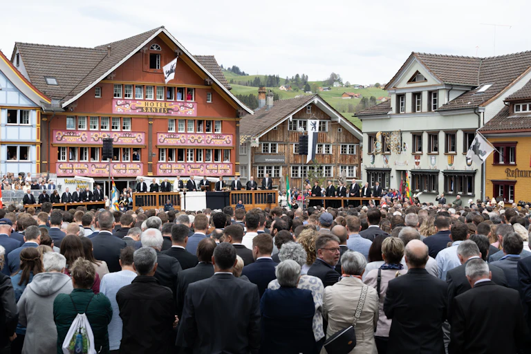 Foule assemblée sur une place, en arrière-plan, sur la tribune les conseillers du canton.