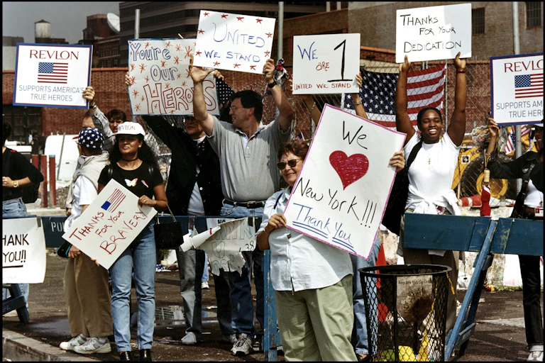 A group of people hold signs that read 'You're Our Heroes,' 'United We Stand' and 'Thanks for Your Bravery.'