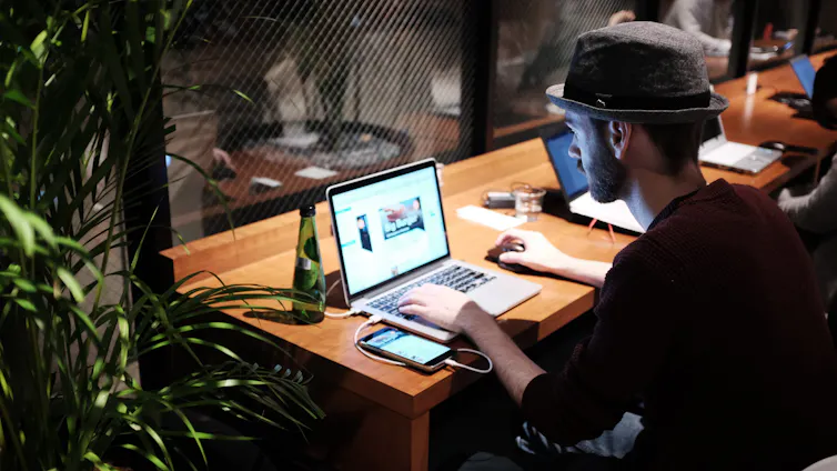 Young man sits at an office desk using a laptop at night