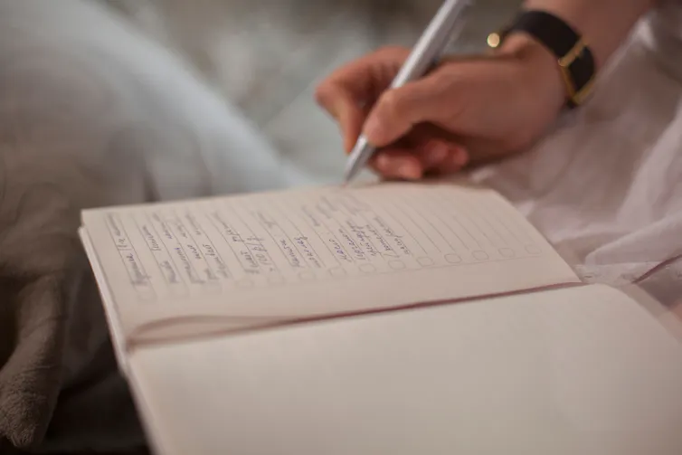 Image of a notebook and a hand holding a pen, writing in it.