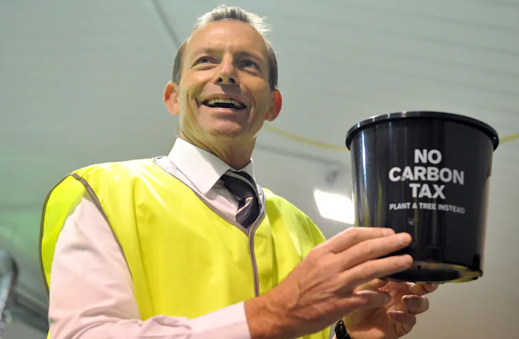 Tony Abbott smiles for the camera while holding a bucket that says no carbon tax