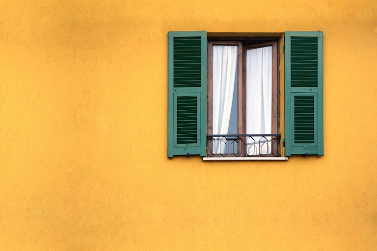 A bright yellow wall with a window with green shutters