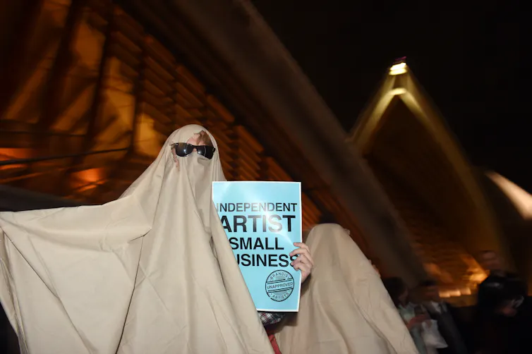 Someone in a ghost costume, holding a sign saying 'independent artist, small business'.
