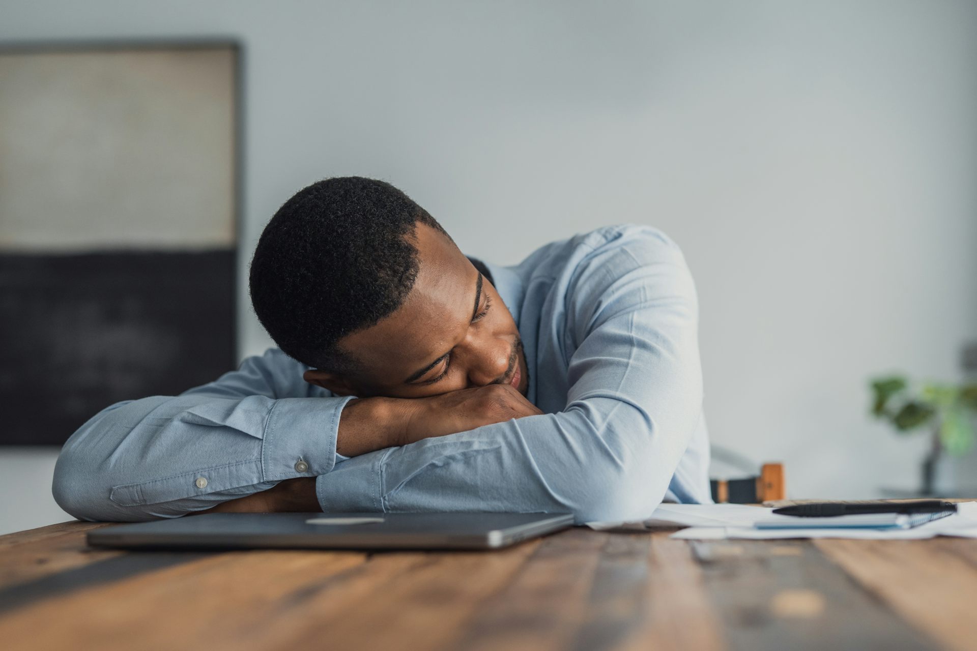 A business man naps on top of his laptop.