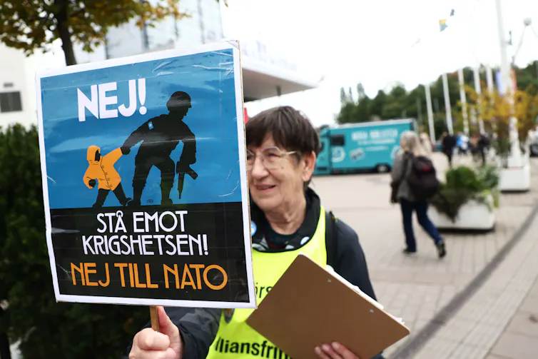 swedish woman holding up a placard showing a child being pulled by a dark figure, protesting at swedish accession to nato