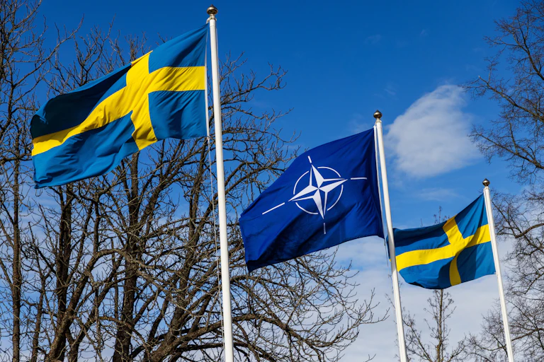 Nato flag flies between two swedish flags against a blue sky.