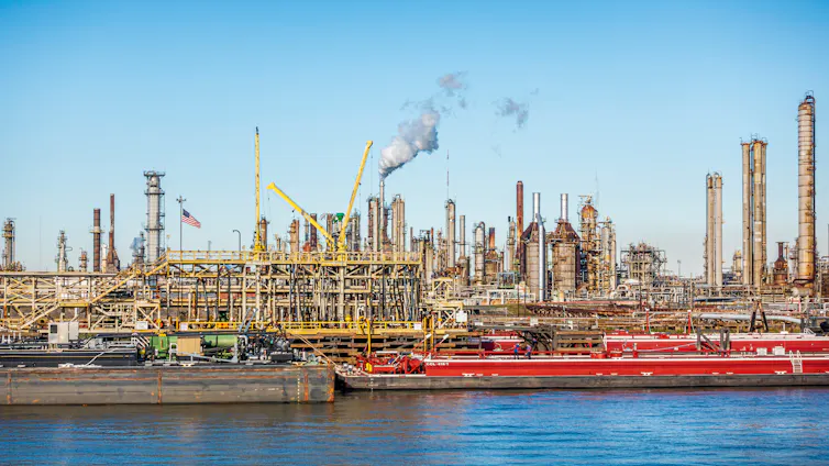 Vista de un complejo industrial junto a un río, donde flotan barcos.
