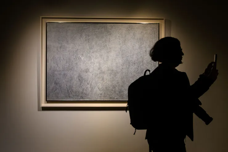 Silhouette of person standing in front of a framed painting that, from a distance, appear to be uneven swaths of grey