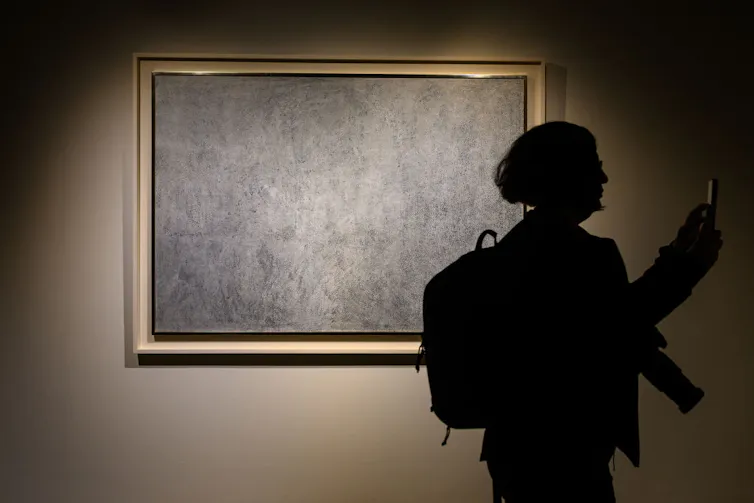 Silhouette of person standing in front of a framed painting that, from a distance, appear to be uneven swaths of grey