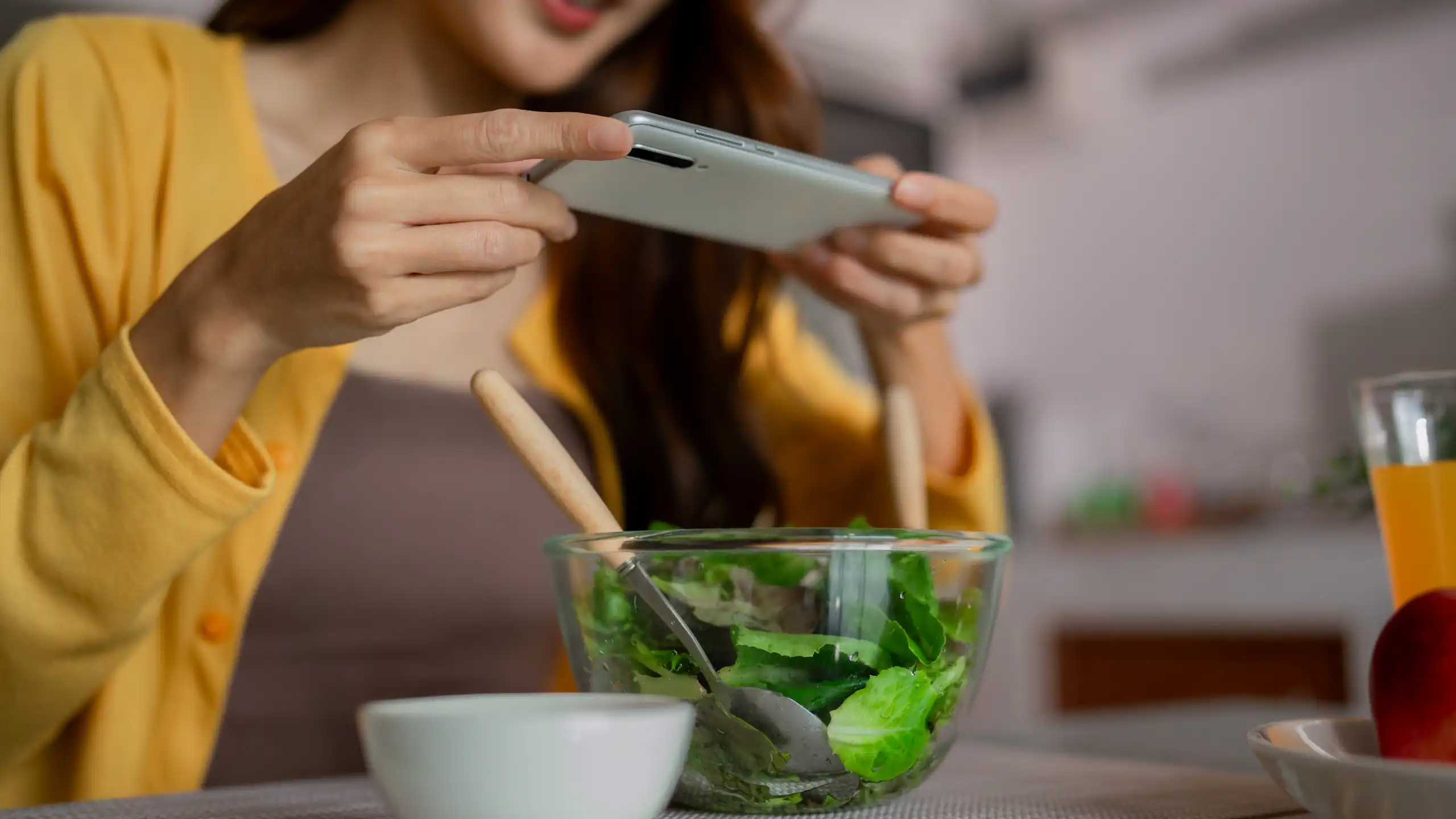 Une jeune femme prend en photo avec son smartphone le bol de salade qu'elle a devant elle.