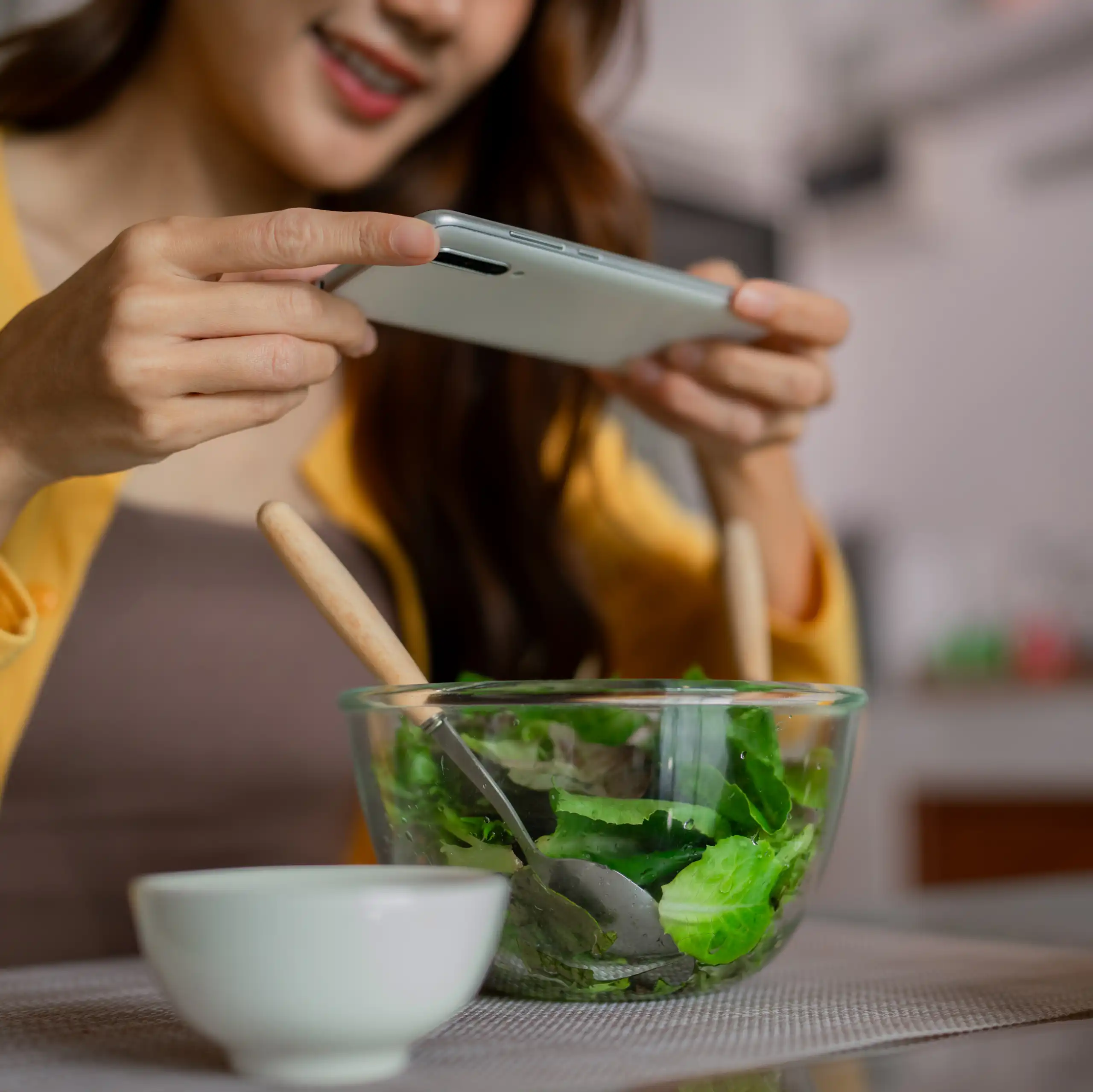 Une jeune femme prend en photo avec son smartphone le bol de salade qu'elle a devant elle.