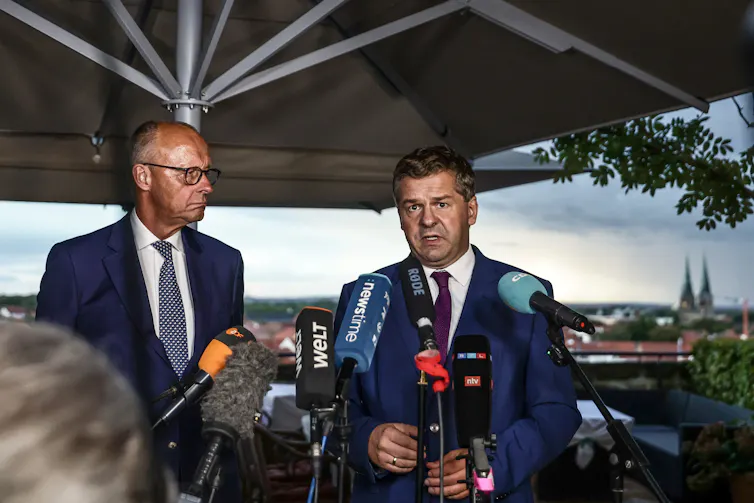 Friedrich Merz looks on as Sven Schulze speaks during a press conference.