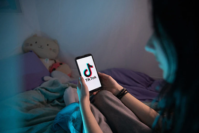 A girl holds a smartphone with the TikTok app logo on the screen.