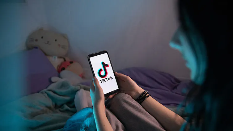 A girl holds a smartphone with the TikTok app logo on the screen.