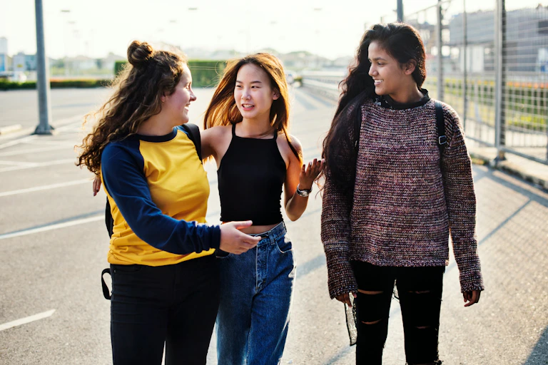 Three teen girls walk and talk and one has her eyes closed.