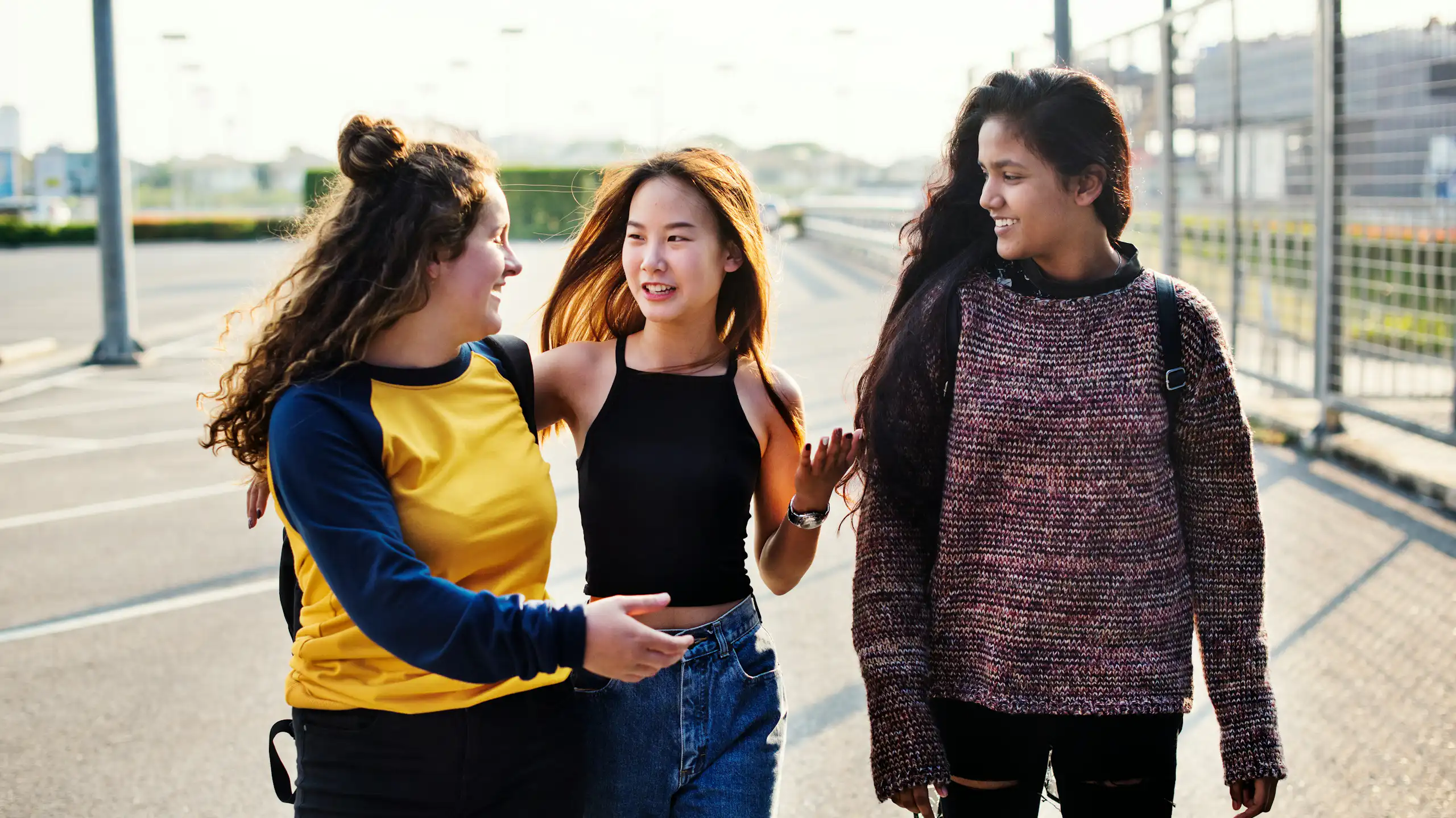 Three teen girls walk and talk and one has her eyes closed.