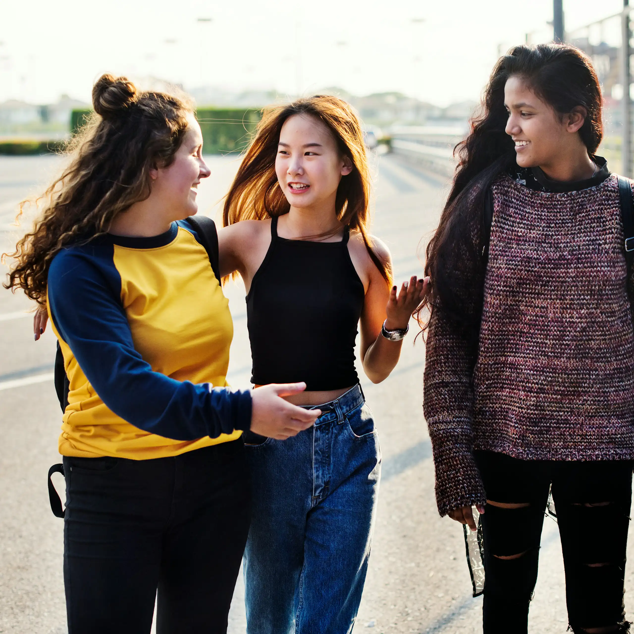 Three teen girls walk and talk and one has her eyes closed.