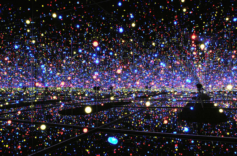 A dark expanse made of mirrors, multicolored circles of light filling the seemingly cavernous space