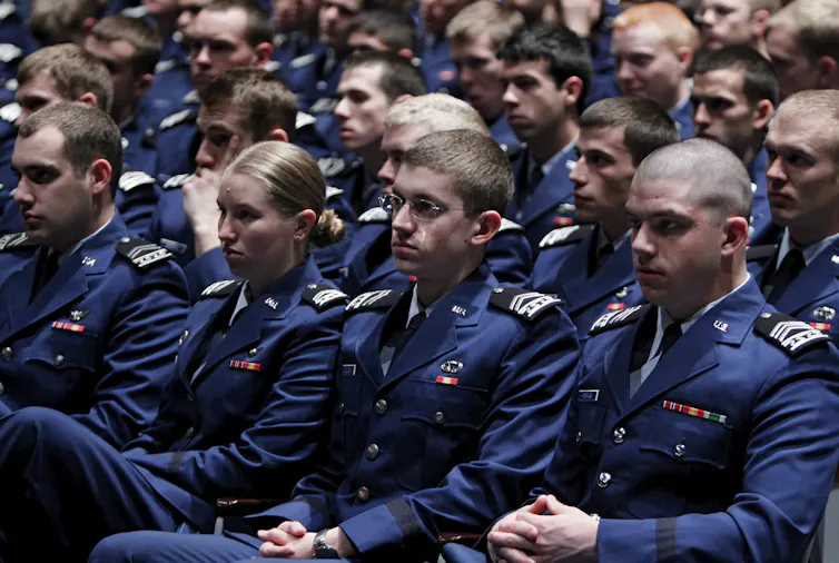 Rows of young people in blue uniforms sit and listen
