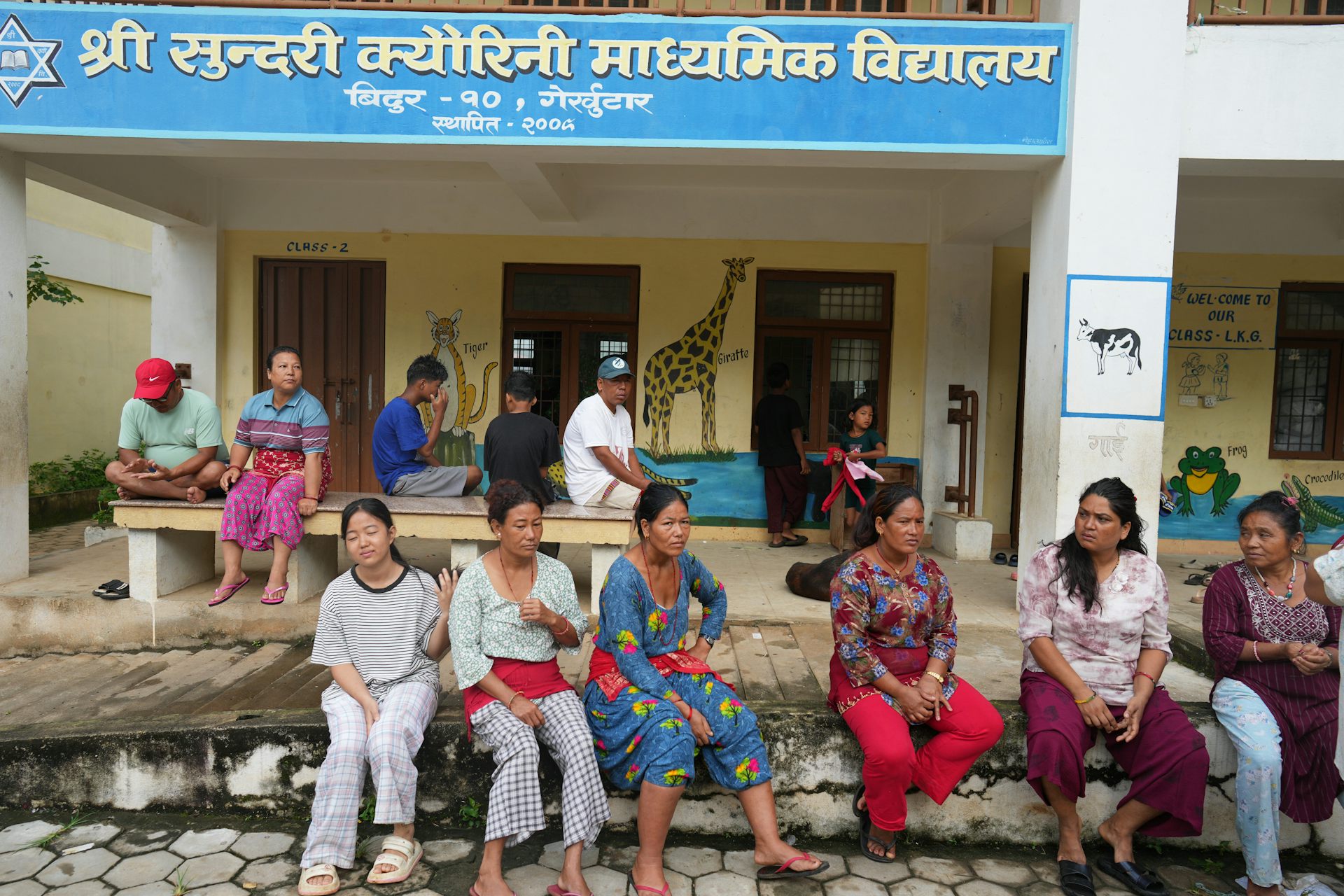 People sit outside a school that has been turned into a temporary shelter, after the devastating Nepal-Tibet floods.