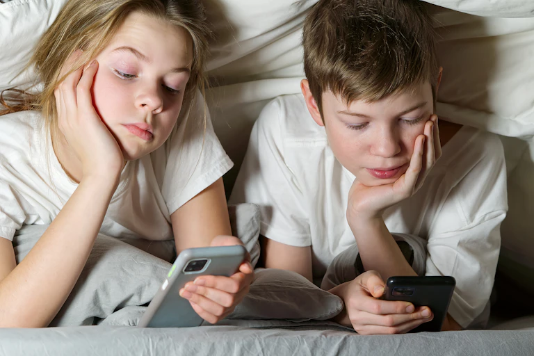 Duas crianças olham smartphones sob um cobertor