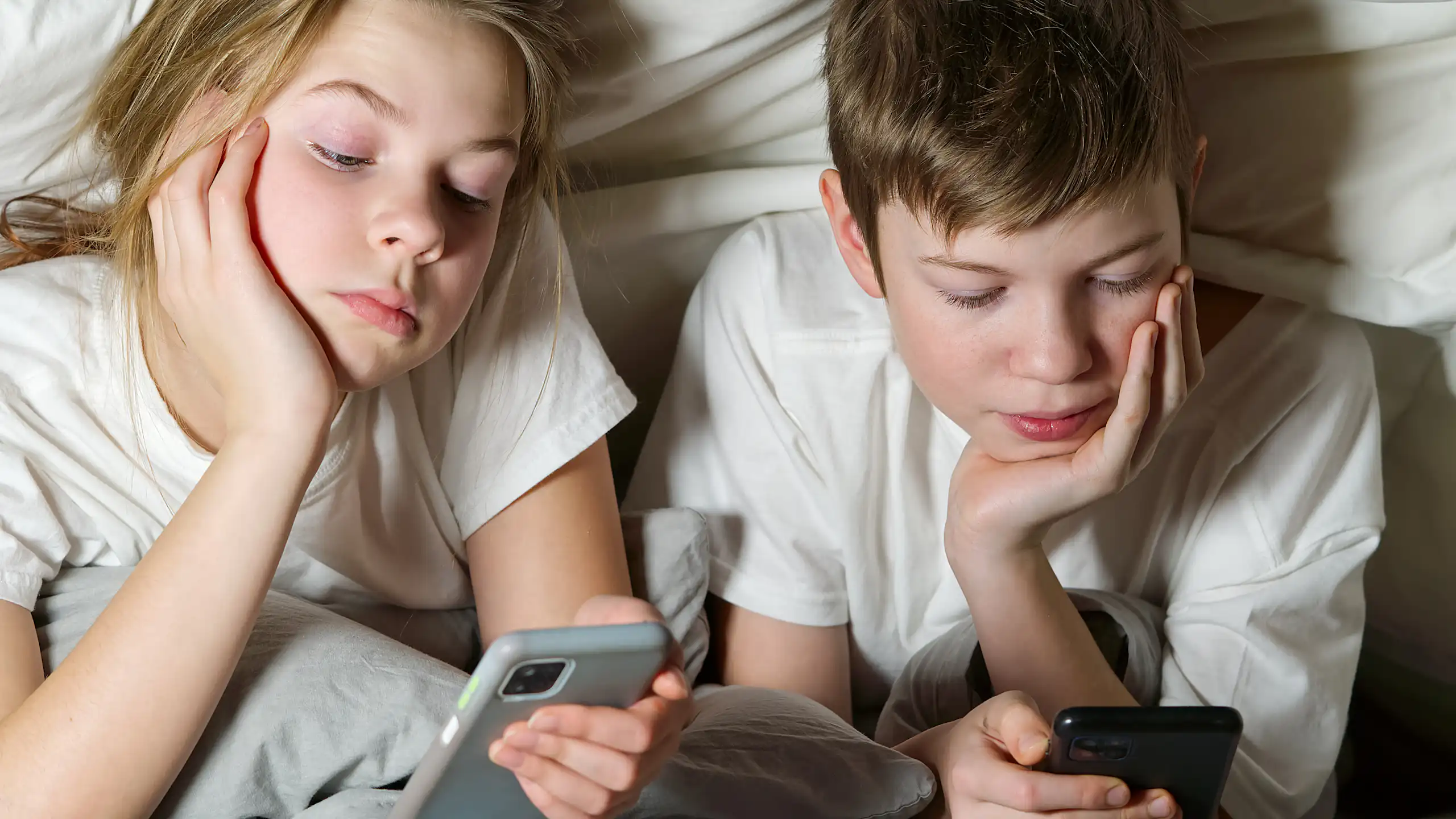 Duas crianças olham smartphones sob um cobertor