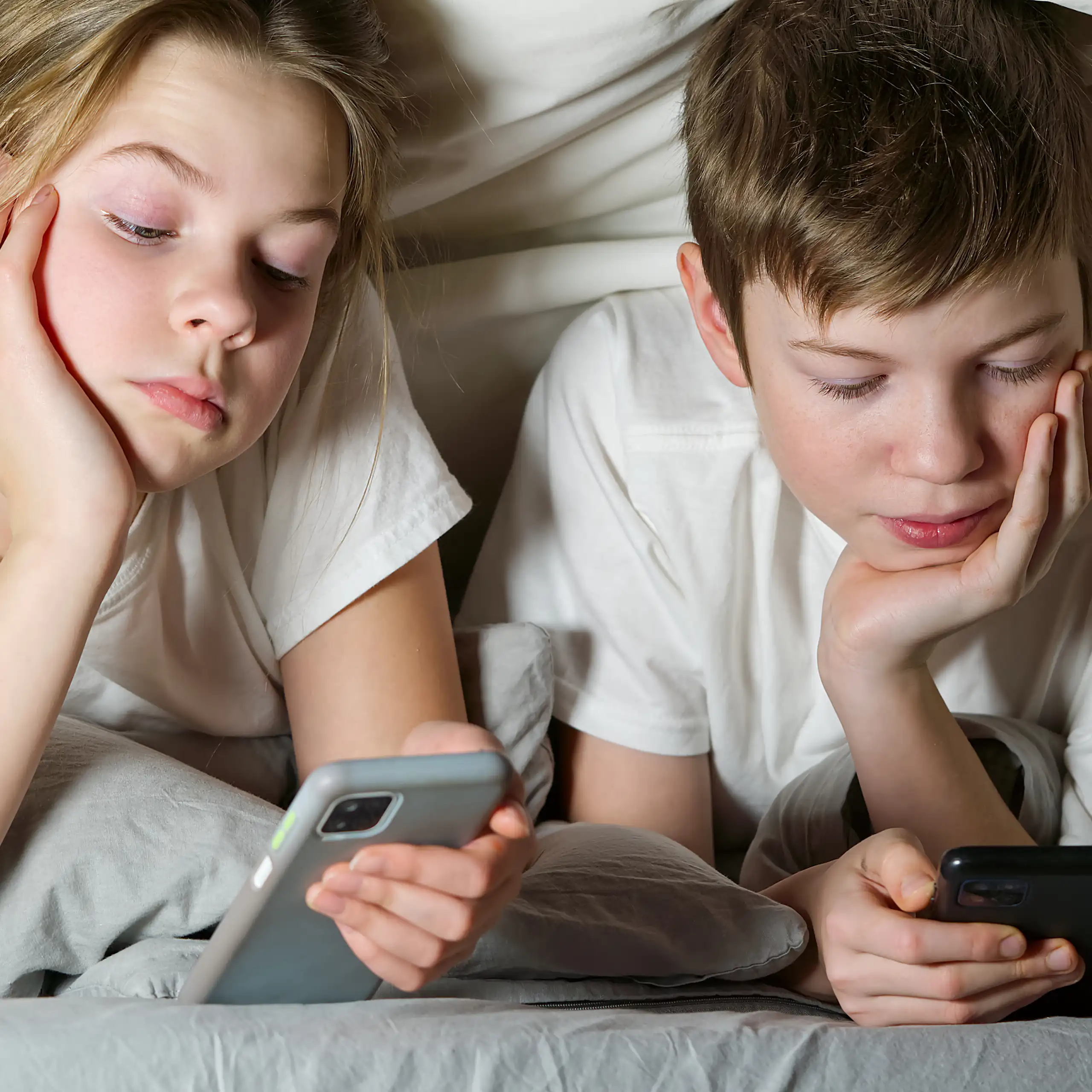 Duas crianças olham smartphones sob um cobertor