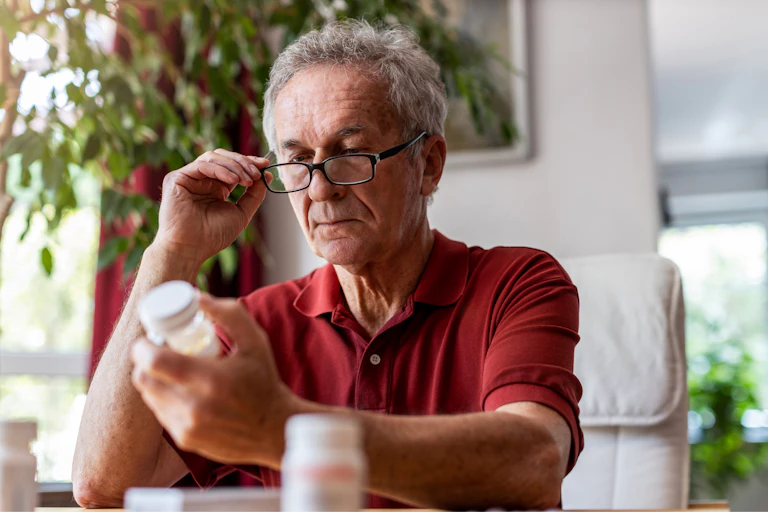 Older man looks at pill bottles.