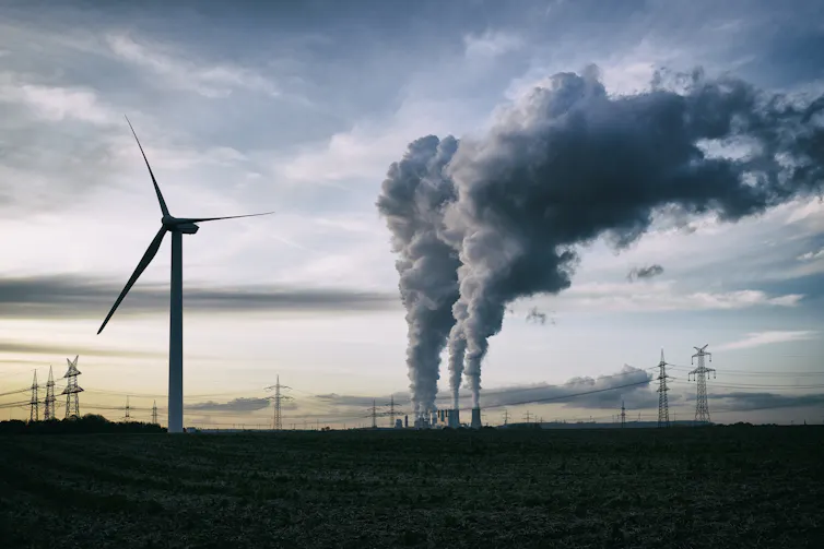 wind turbine and coal plant seen at a distance, grey sky.