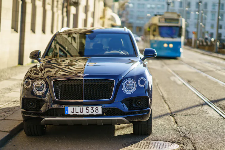 black bentley parked at the side of a road in gothenburg, sweden, with a tram approaching in the distance.
