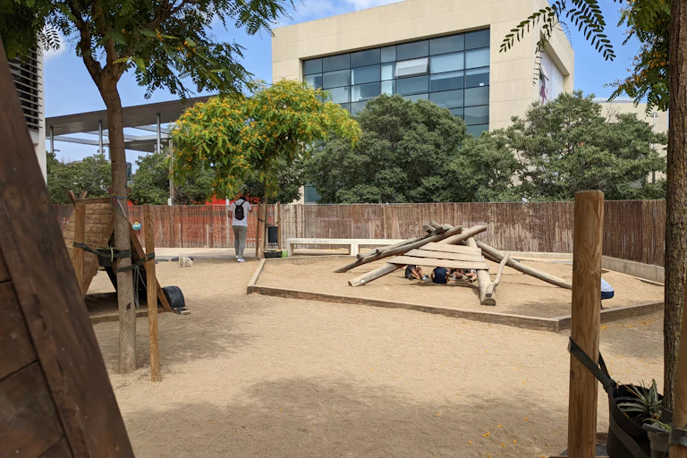 Uns infants juguen sota una estructura de fusta a un pati amb arbres.