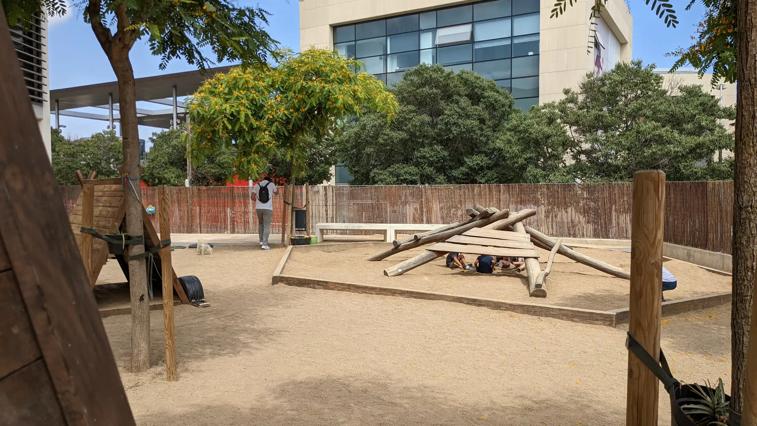 Uns infants juguen sota una estructura de fusta a un pati amb arbres.