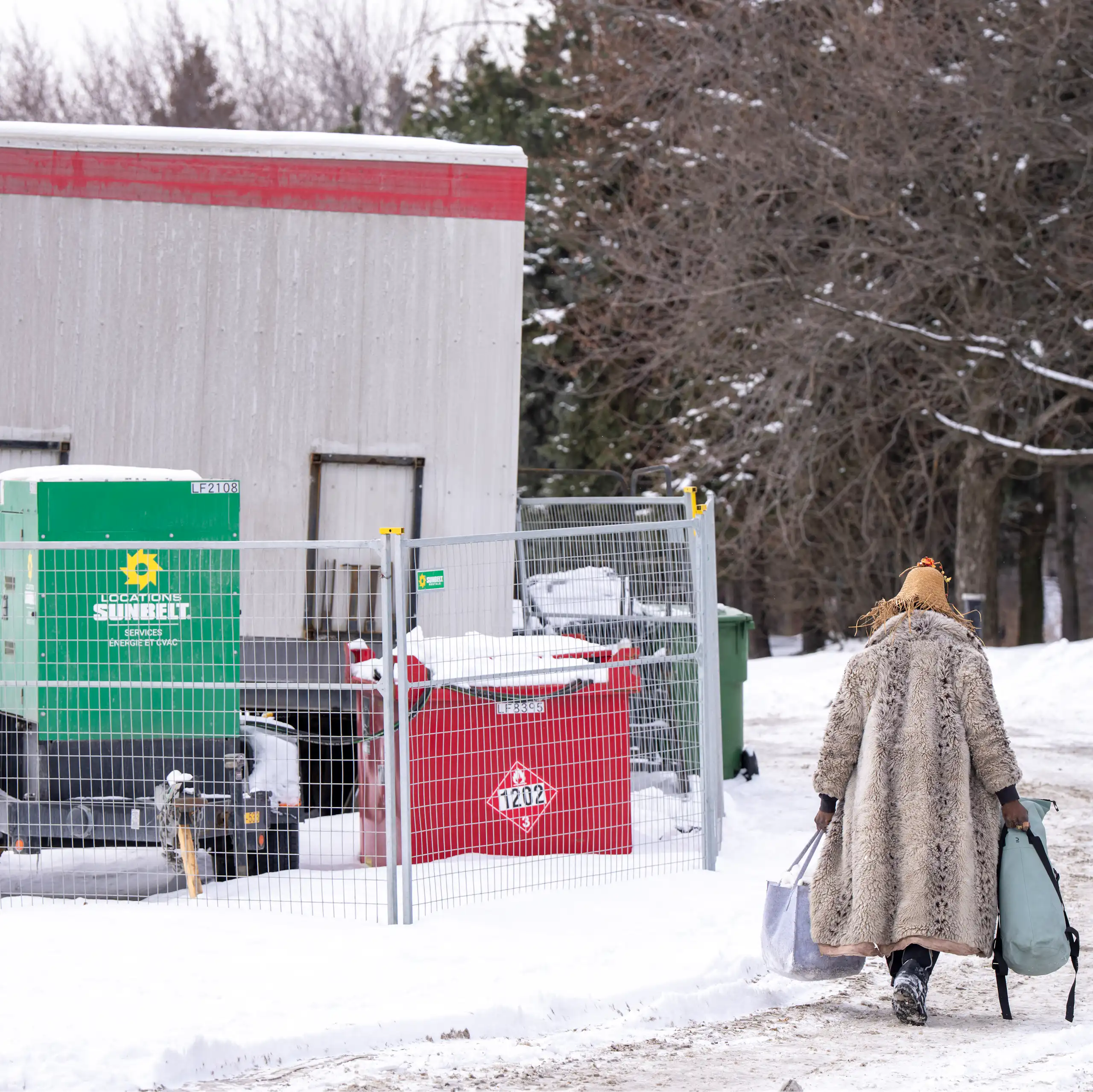 Une femme vue de dos, vêtue d'un manteau, transporte des sacs qui contiennent ses possessions.