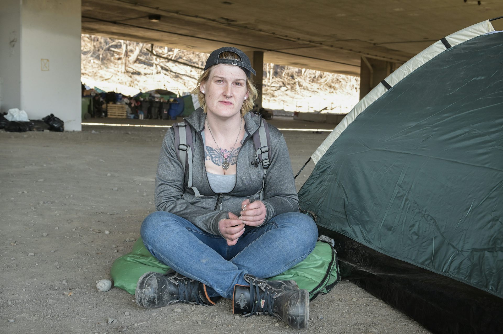 Une femme pose à côté de sa tente, installée sous un viaduc