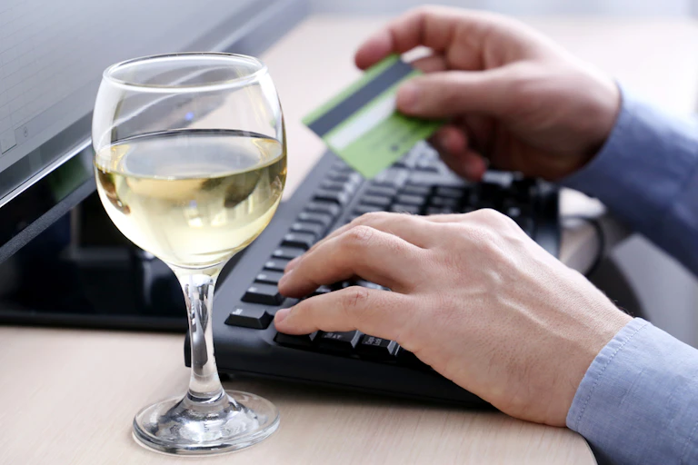 Person orders goods on their computer with glass of wine next to the keyboard
