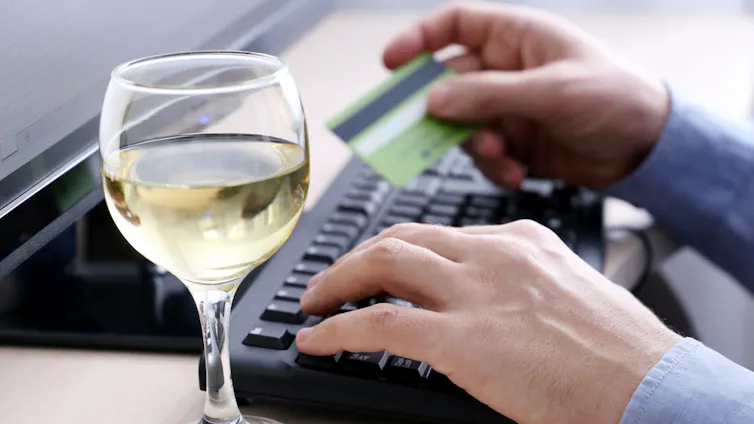 Person orders goods on their computer with glass of wine next to the keyboard