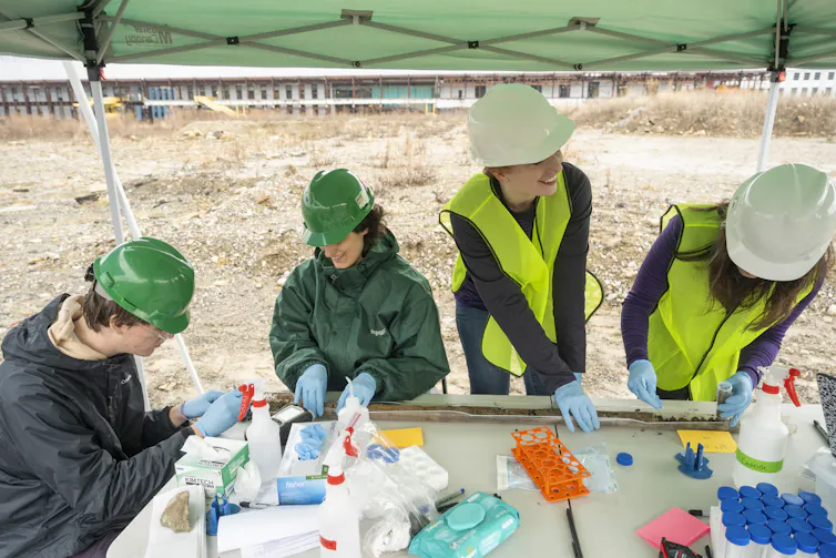 Four people work in an open field with scientific samples.