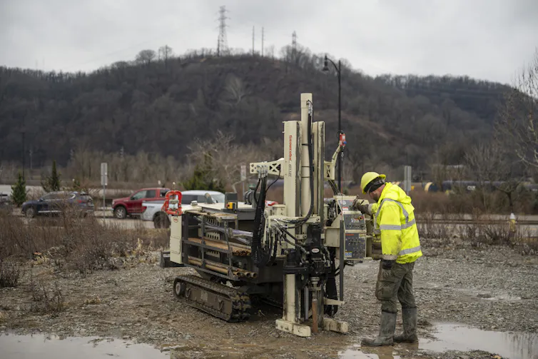 A large machine is operated by a man wearing a neon yellow hat and vest.