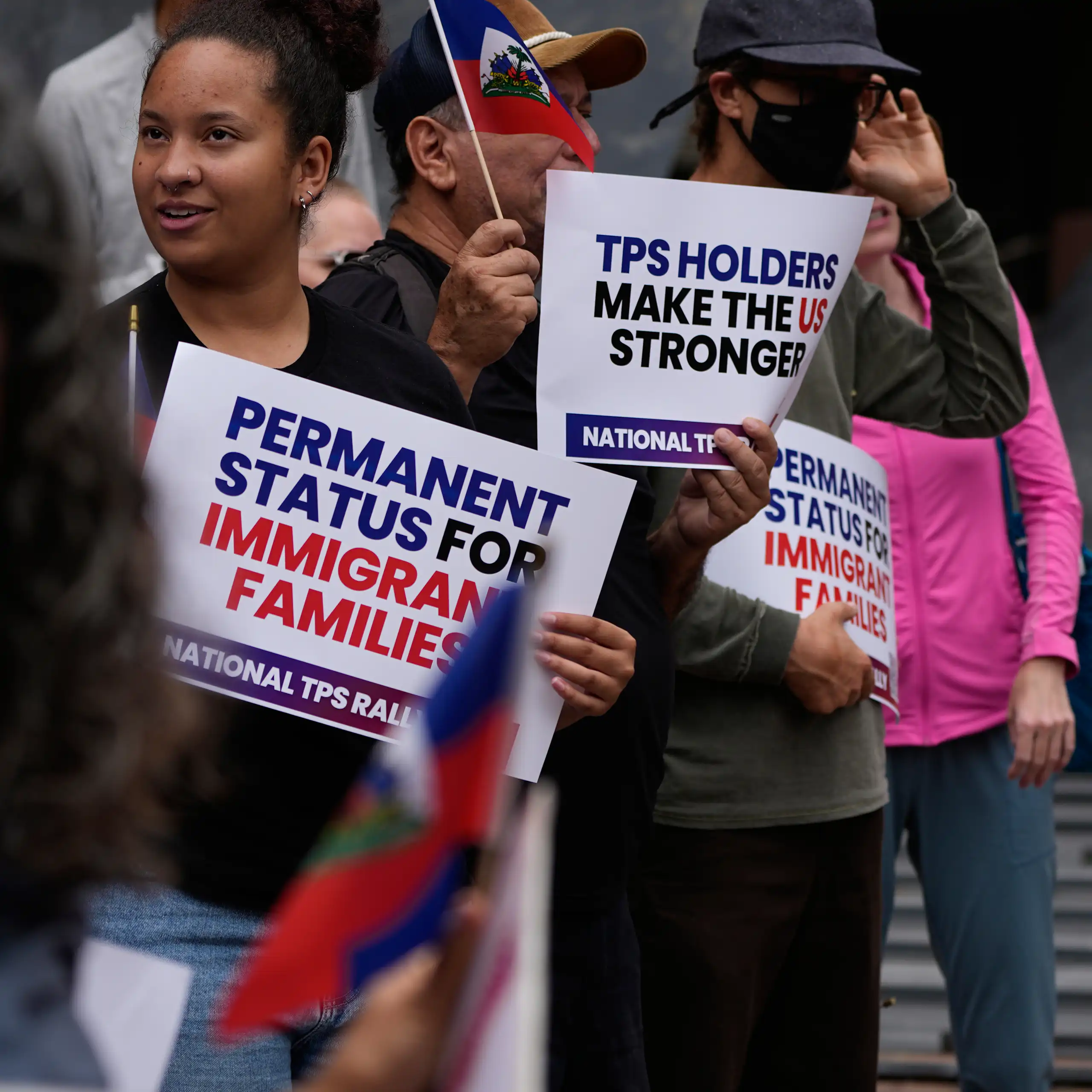 People at a rally hold signs that say 'permanent status for immigrant families' and 'TPS holders make the US stronger.'