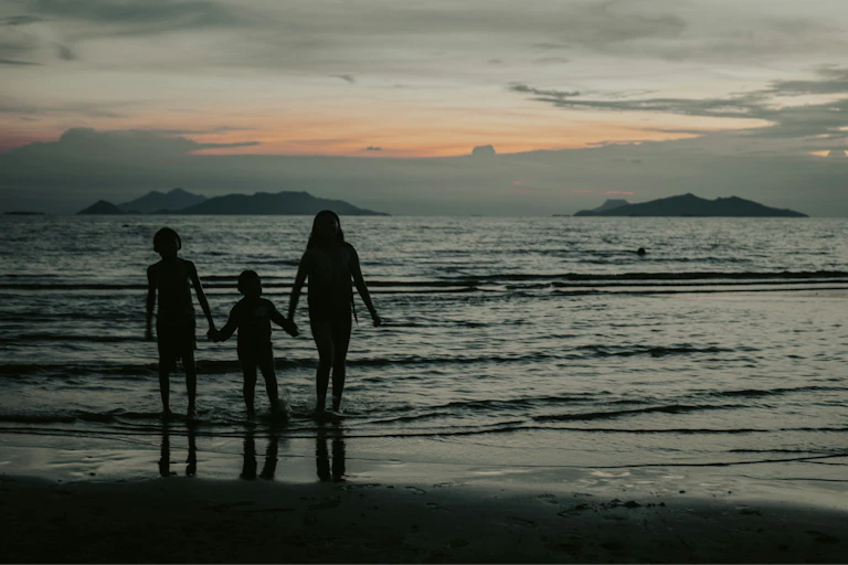 A beach sunset with the silhouettes of three people walking hand in hand