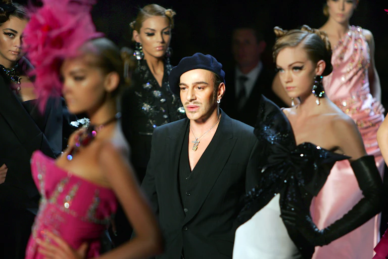 Close up of a designer in black clothing and models posing on a fashion runway.