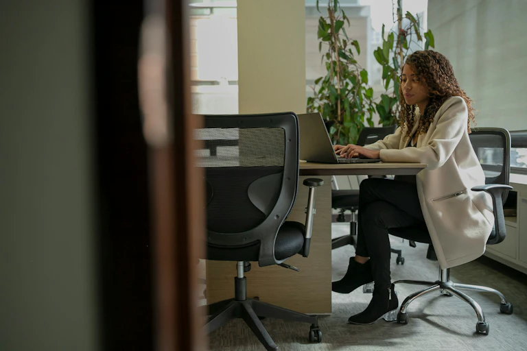 Woman sits at an office desk typing on a laptop.