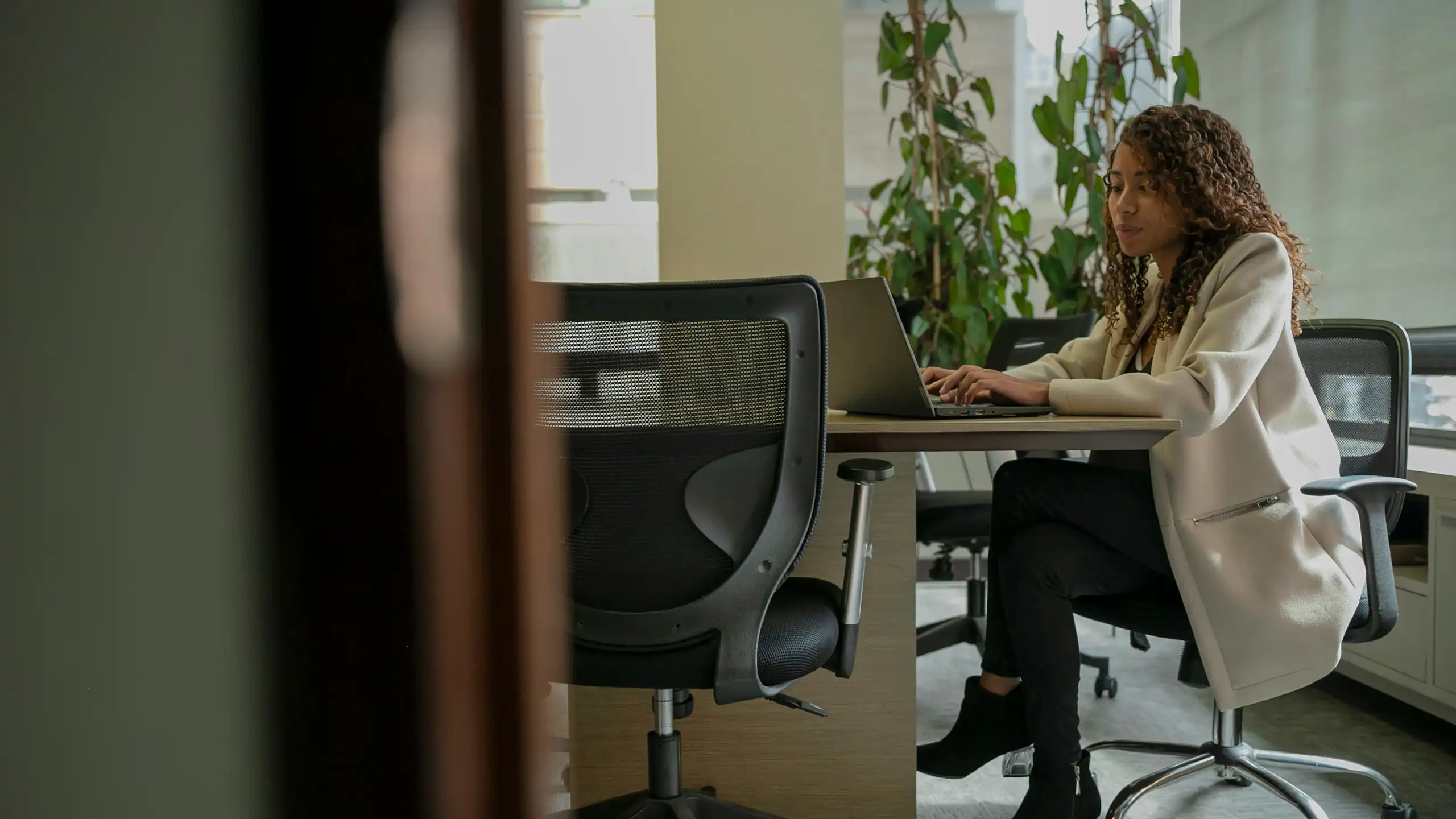 Woman sits at an office desk typing on a laptop.