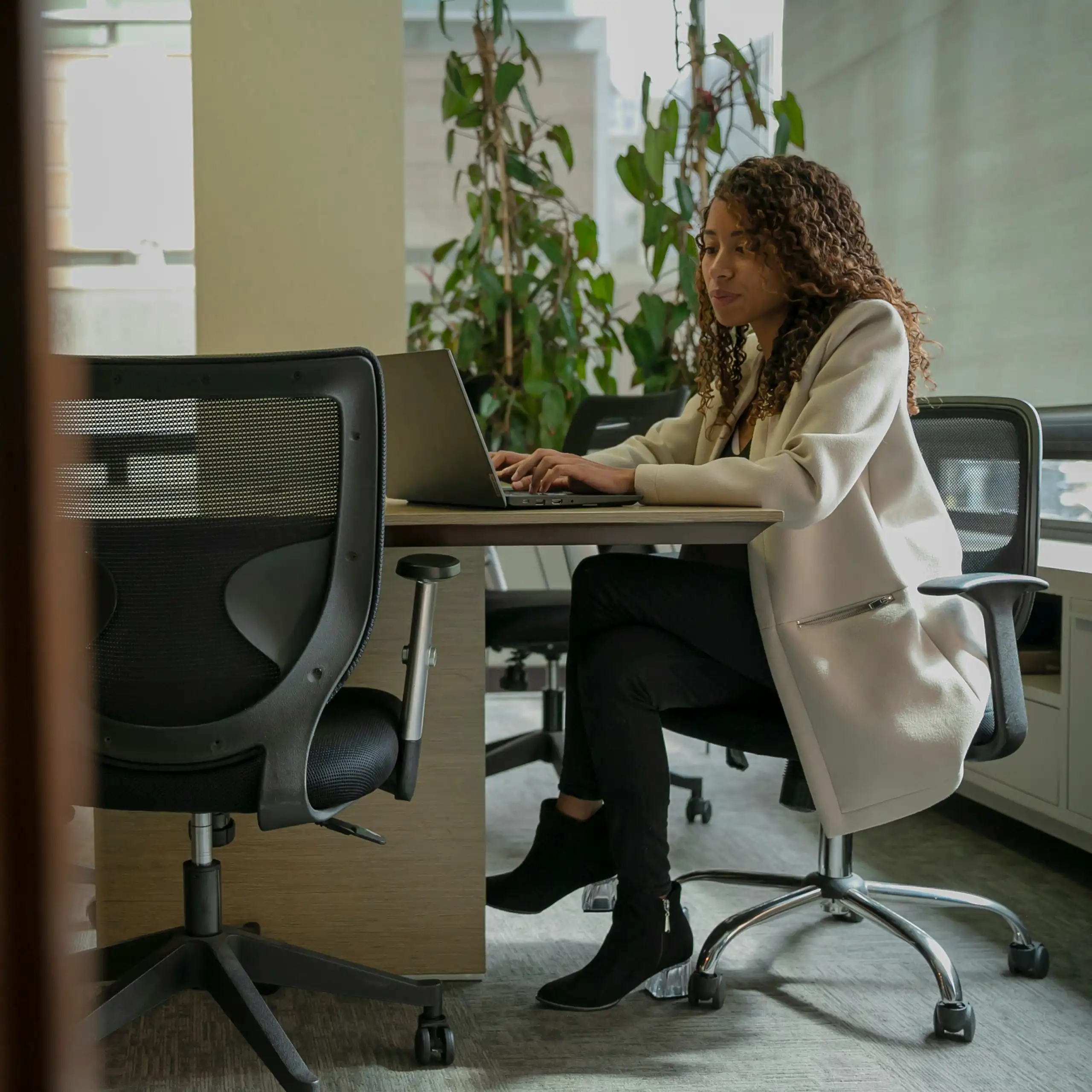 Woman sits at an office desk typing on a laptop.