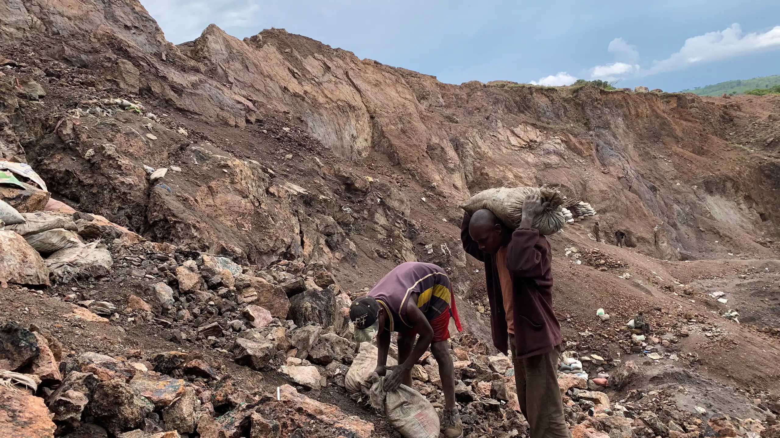 Two people in a dug up and rocky area stuffing sacks