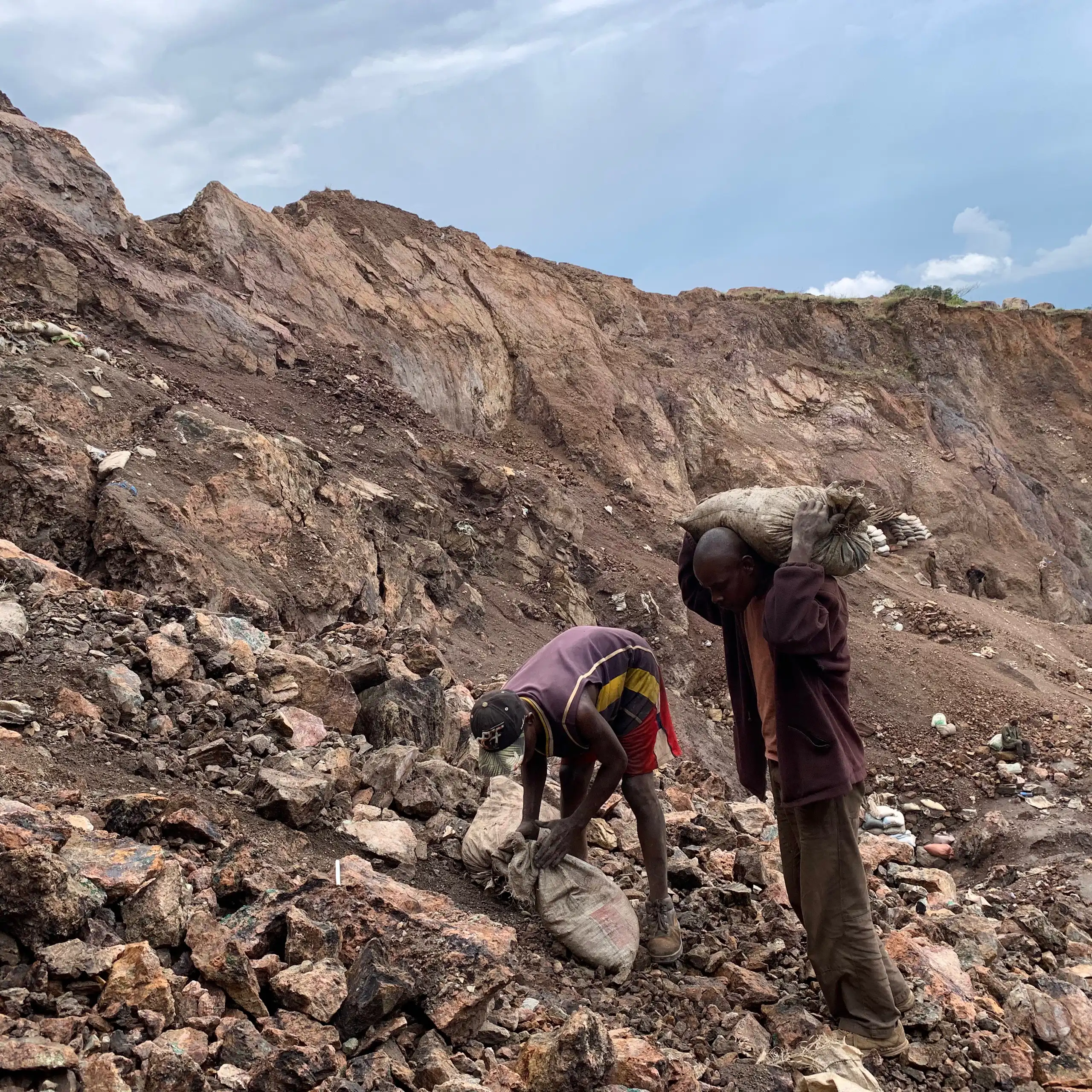 Two people in a dug up and rocky area stuffing sacks