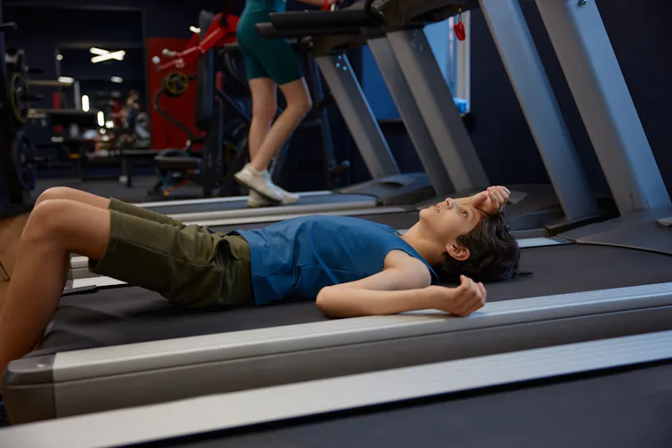 A tired woman lays on a treadmill.