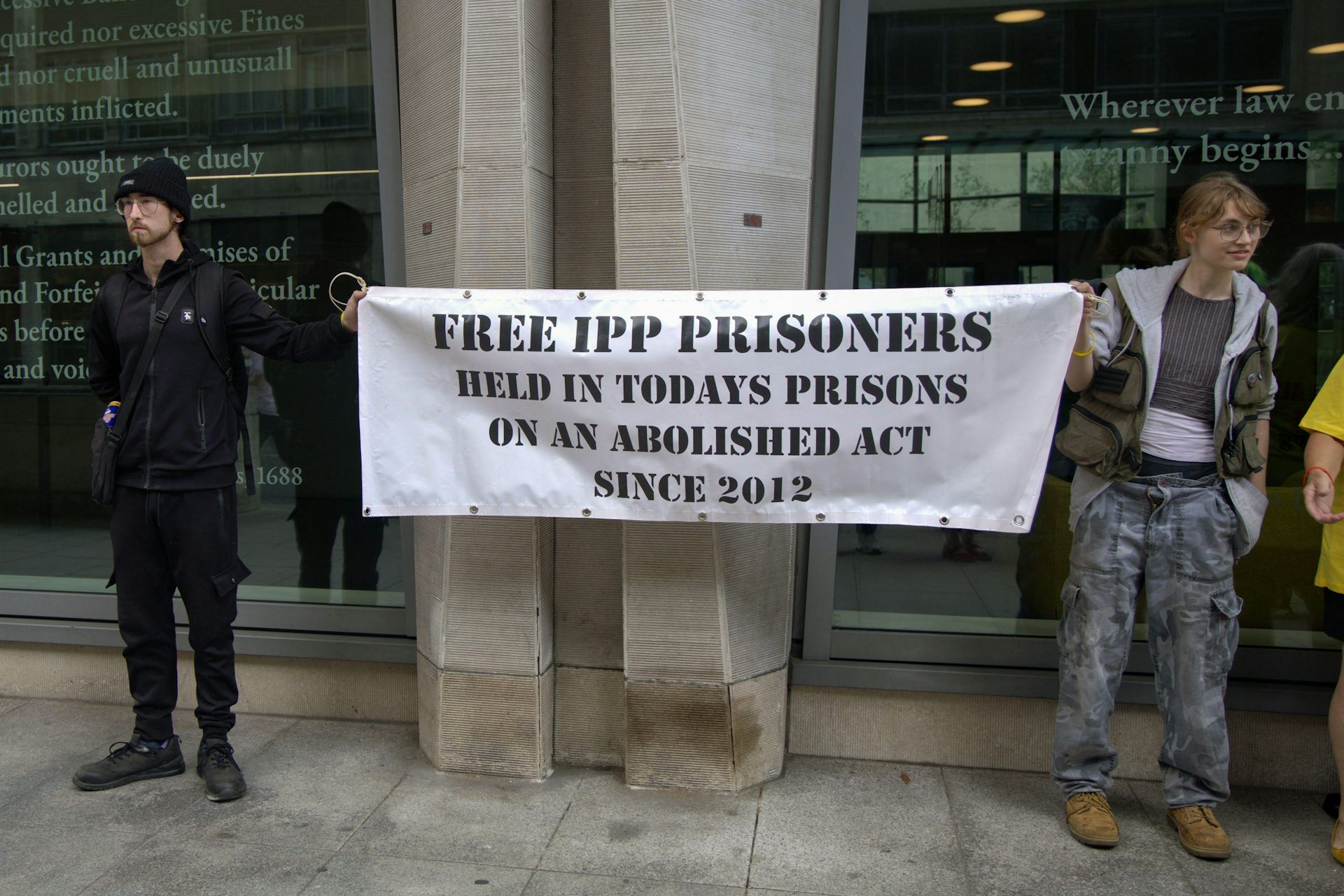 Two people holding a banner that reads 'free IPP prisoners, held in today's prisons on an abolished act since 2012'