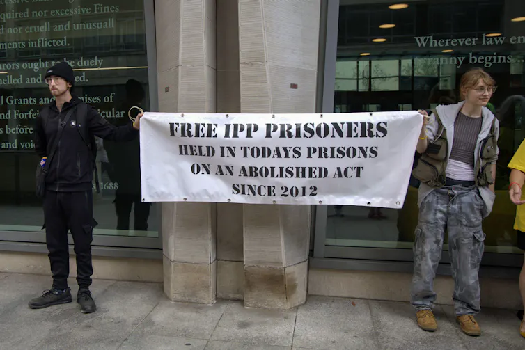 Two people holding a banner that reads 'free IPP prisoners, held in today's prisons on an abolished act since 2012'