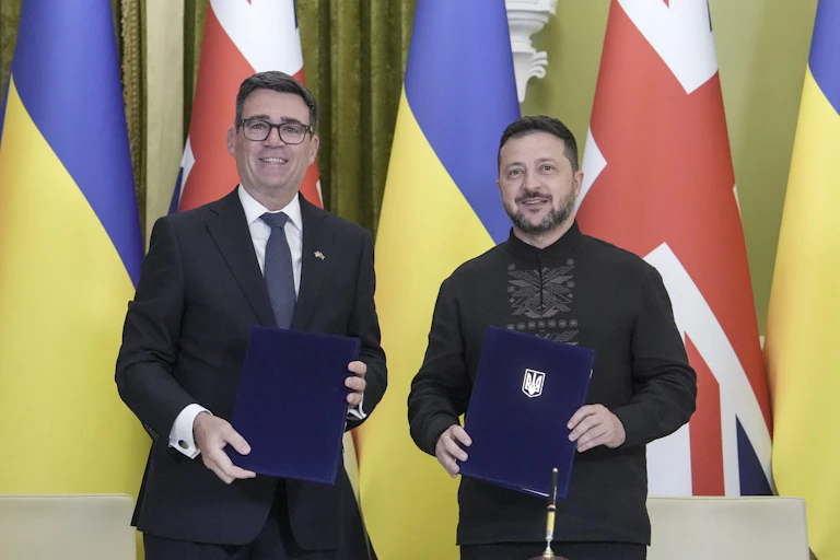 UK prime minister Andy Burnham with Ukrainian prime minister Volodymyr Zelensky in front of UK and Uklraininan flags. Both are holding folders.